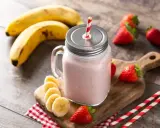 Un délicieux smoothie fraise banane dans un bocal en verre, garni de fruits frais et de pailles rayées.