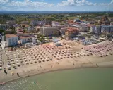 Vista aerea di una spiaggia affollata con ombrelloni rosa e bianchi, hotel e case nel centro storico di Torre Pedrera.