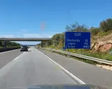Autobahn A22 in Portugal. Ein Auto fährt auf der rechten Spur, vorbei an einem Schild mit Zielen wie Portimão und Lagos.