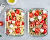 Zwei Glasbehälter mit frischen Mahlzeiten: links Nudelsalat, rechts ein bunter Quinoa-Salat mit Tomaten und Mozzarella.