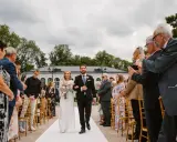 Para młoda idzie alejką, goście robią zdjęcia. Formalności po ślubie w pełni.