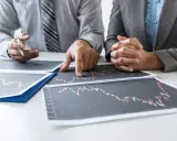 Dwóch biznesmenów analizuje wykresy, omawiając strategię finansową, być może dotyczącą kredytu pomostowego.