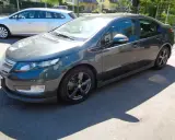 Ciemnoszary Chevrolet Volt stoi na parkingu. Obok niego widać srebrne kombi.