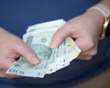 Dłonie trzymające polskie banknoty 100 zł. Czy to nagroda, czy może podatek od nagrody?