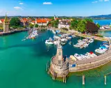 Malowniczy port nad Jeziorem Bodenskim z licznymi jachtami, latarnią morską i zabytkową zabudową miasta.