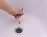 Mano retirando pelos y suciedad del desague plano de una bañera con un bolígrafo.