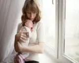 Zmęczona mama tuli płaczące dziecko, które właśnie robi kupę w nocy.