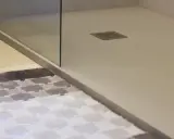 Plato de ducha de resina con desagüe cuadrado. Alfombra a cuadros en primer plano.