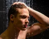 Ein Mann unter der Dusche, der sich die Haare wäscht. Die kalte Dusche ist eine Herausforderung, aber er hält durch.