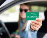 Mujer con gafas de sol muestra tarjeta "INTENSIVO" de autoescuela. Obtener el carnet B+E es difícil, pero este curso intensivo puede ayudar.