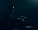 Mężczyzna w ciemnym pomieszczeniu, siedzi w fotelu. Jego sylwetka jest ledwo widoczna, podkreślona przez subtelne światło. To idealny przykład low key fotografii.