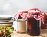 Gläser mit Erdbeermarmelade, bereit zum Marmelade einfrieren. Daneben ein Becher und frische Walderdbeeren.
