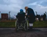 Accompagnamento anziani a chi spetta: una donna spinge una persona in sedia a rotelle, con altre figure sfocate sullo sfondo.