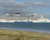 A large white MSC World Europa cruise ship docked next to a blue tanker ship in the sea.