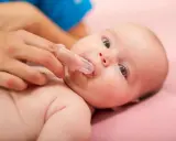 Delikatne czyszczenie ząbków niemowlaka specjalną nakładką na palec. Pokazuje, jak myć zęby niemowlakowi.