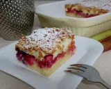Szybkie kruche ciasto z owocami i pianką, posypane cukrem pudrem, czeka na widelczyku. Obok blaszka z resztą wypieku i rabarbar.