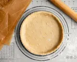 Pâte sucrée noisette prête à être garnie, sur un tapis de pâtisserie avec un rouleau à bois et du papier sulfurisé.
