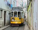 Gelbe straßenbahn lissabon fährt durch enge Gasse, Wäsche hängt über der Straße.