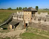 Rekonstrukcja grodziska w Tumie z drewnianą wieżą i palisadą. Widać schody prowadzące na wały i mały budynek.