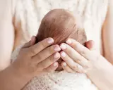Mani delicate che accarezzano la testa di un neonato, proteggendo la sua fontanella.