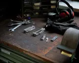 Variedad de accesorios multiherramienta, llaves inglesas, guantes y auriculares sobre una mesa de trabajo.