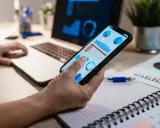 Una gestora de fondos revisa gráficos financieros en su móvil y portátil, analizando datos para tomar decisiones estratégicas.