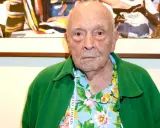 An elderly man with a green jacket over a floral shirt. This image might spark some david bailey interesting facts about his iconic style.