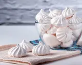 Douceur aérienne : des meringues délicates, comme préparées au bain-marie, dans un bol en verre et sur un tissu texturé.