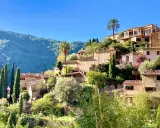 Malerische Häuser mit Zypressen und Palmen, ein grüner Berghang im Hintergrund. Ein friedlicher Anblick von Mallorca im Dezember.