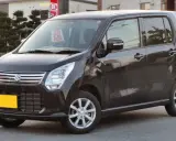 Ciemny Suzuki Wagon R+ z żółtą tablicą rejestracyjną, zaparkowany na ulicy.