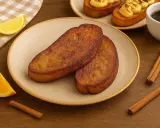 Dos torrijas doradas en un plato, acompañadas de gajos de naranja y limón, canela y café. ¡La mejor receta de torrijas!