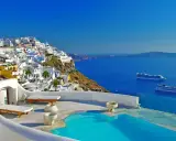 Vista mozzafiato di Santorini con case bianche a picco sul mare blu intenso. Due navi da crociera all'orizzonte, un invito a scoprire crociere a prezzi stracciati.