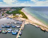 Władysławowo co zobaczyć: port z łodziami, szeroka plaża pełna turystów i miasto w tle. Idealne miejsce na wakacje nad morzem.