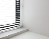 Białe żaluzje poziome na oknie, idealne, by pokazać, jak dobrać roletę do okna. Minimalistyczne wnętrze.