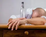 Mężczyzna śpi na stole obok pustej butelki. Zastanawiasz się, co wypić przed alkoholem, by uniknąć takiego losu?