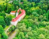 Zamek na skale w Trzebieszowicach, otoczony bujną zielenią, malowniczo wznosi się nad rzeką.