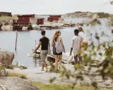 Vänner njuter av en promenad längs vattnet vid röda fiskestugor, en perfekt bild av eco tourism i Sverige.