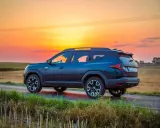 Ciemnoniebieski Dacia Bigster 2025 na tle zachodzącego słońca, na wiejskiej drodze.