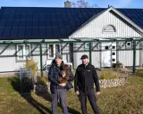 Två män och en hund framför ett hus med solpaneler på taket. Taket har vackra vinklar som ger huset karaktär.