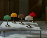 Fem färgglada lampor i Verner Panton-stil står på ett vitt bord framför en lädersoffa.