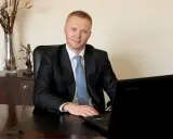 Mężczyzna w garniturze siedzi przy biurku z laptopem, obok statuetka Temidy.