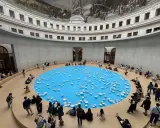 A circular room with a frescoed ceiling, featuring a bright blue pool dotted with white ceramic bowls. Visitors observe this installation, part of the François-Henri Pinault art collection.
