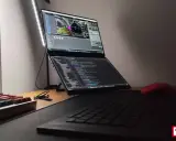 Na biurku laptop z dwoma ekranami, na górnym widać scenę w Unreal Engine 6, na dolnym kod. Obok klawiatura i czerwona myszka.