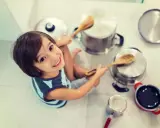 Niño sonriente jugando con ollas y cucharas de madera, creando sus propios instrumentos musicales caseros.
