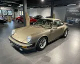 Ein goldener Porsche 911 SC 3.0 steht in einer Ausstellungshalle, flankiert von anderen Sportwagen.