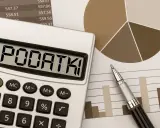 Kalkulator z napisem "PODATKI" obok wykresów i długopisu. Obliczenia podatku od sprzedaży działki.