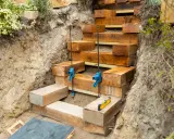 Construction d'un escalier en bastaing dans une pente. Des serre-joints bleus maintiennent les poutres en bois pendant que le niveau à bulle assure la précision.
