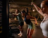 Drei Personen machen ein intensives AMRAP Workout an Kabelzügen. Sie ziehen die Griffe nach hinten und trainieren so ihren Rücken.