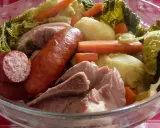 Un plat typique auvergnat : saucisses, porc, pommes de terre, carottes et chou savoyard mijotés dans un grand bol en verre.