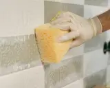 Ręka w rękawiczce czyści gąbką błyszczące kafelki z ozdobnym wzorem.